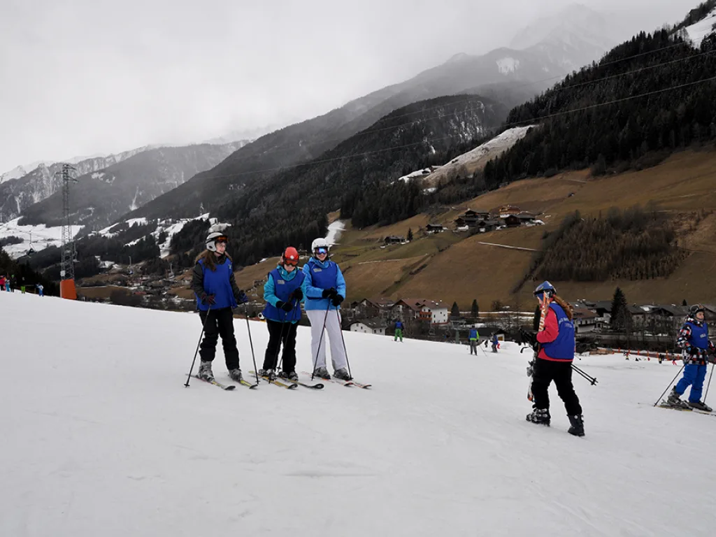 Gruppe steht auf Skiern am Pistenrand, dahinter der Ort im Tal.